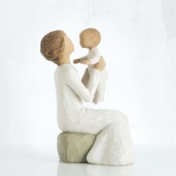 Close view of older figurine sitting on rock holding up baby