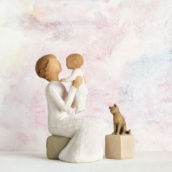 Close view of older figurine sitting on rock holding up baby