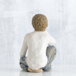 Small boy figurine in white shirt and blue jeans sitting down with one hand on his face