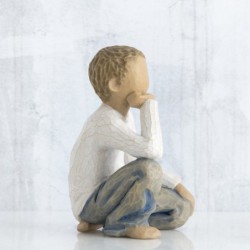 Small boy figurine in white shirt and blue jeans sitting down with one hand on his face