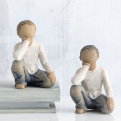 Small boy figurine in white shirt and blue jeans sitting down with one hand on his face