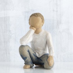 Small boy figurine in white shirt and blue jeans sitting down with one hand on his face