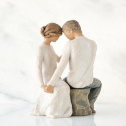 Faceless man and woman figurine sitting on rock wearing all white holding hands