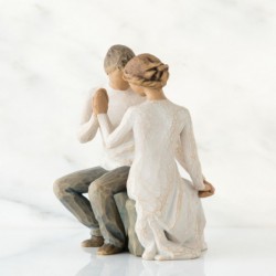 Faceless man and woman figurine sitting on rock wearing all white holding hands