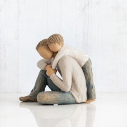 Father figurine sitting down hugging boy figurine from behind - both are wearing blue jeans and white shirts