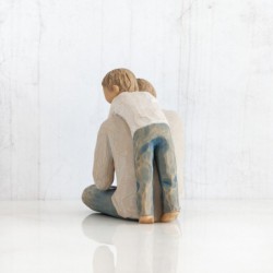 Father figurine sitting down hugging boy figurine from behind - both are wearing blue jeans and white shirts