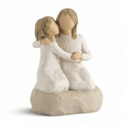 Two small girl figurines in white dresses hugging one another on round rock plaque