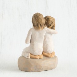 Two small girl figurines in white dresses hugging one another on round rock plaque