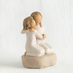 Two small girl figurines in white dresses hugging one another on round rock plaque