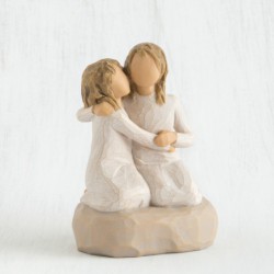 Two small girl figurines in white dresses hugging one another on round rock plaque