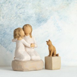 Two small girl figurines in white dresses hugging one another on round rock plaque