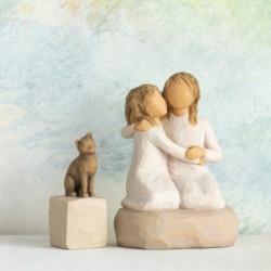 Two small girl figurines in white dresses hugging one another on round rock plaque