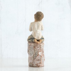 Front view of boy with brown hair sitting on a stump while holding a small potted plant to his chest