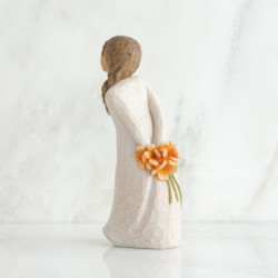RIght side view of girl with brown hair in braid over right shoulder leaning forward as she holds orange flowers behind her back